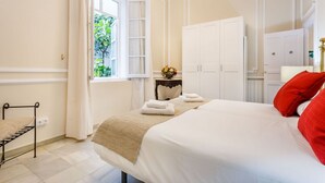 A hotel room with a large bed, a window with curtains, a wardrobe, and a small table with a vase of flowers. - Families, calm city center 3 bedrooms 5 bathrooms wifi air conditioning heating (Sevilla)