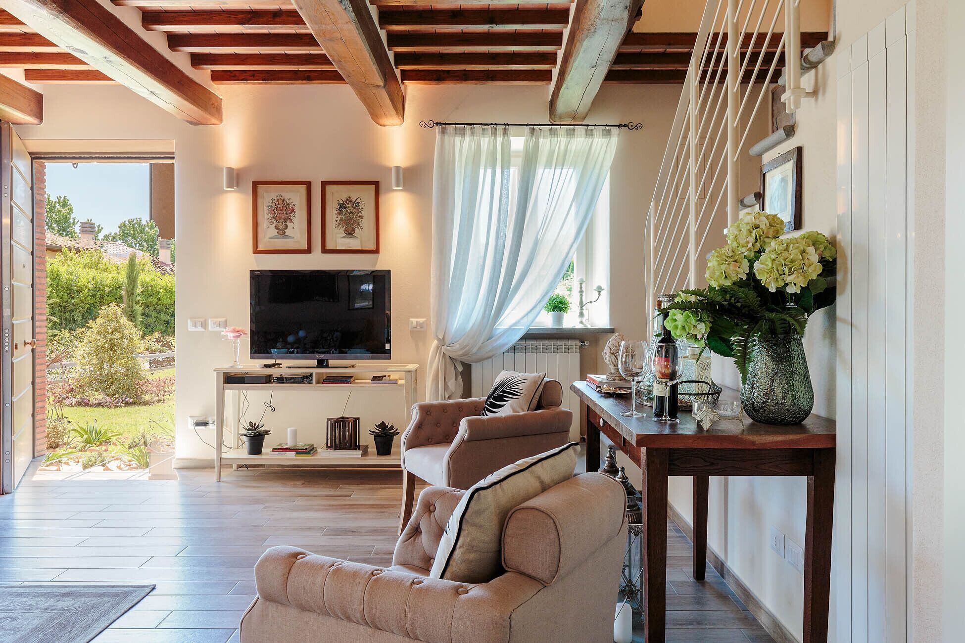 Una sala de estar con televisor, sofá, mesa de comedor con un jarrón de flores y vistas al exterior.