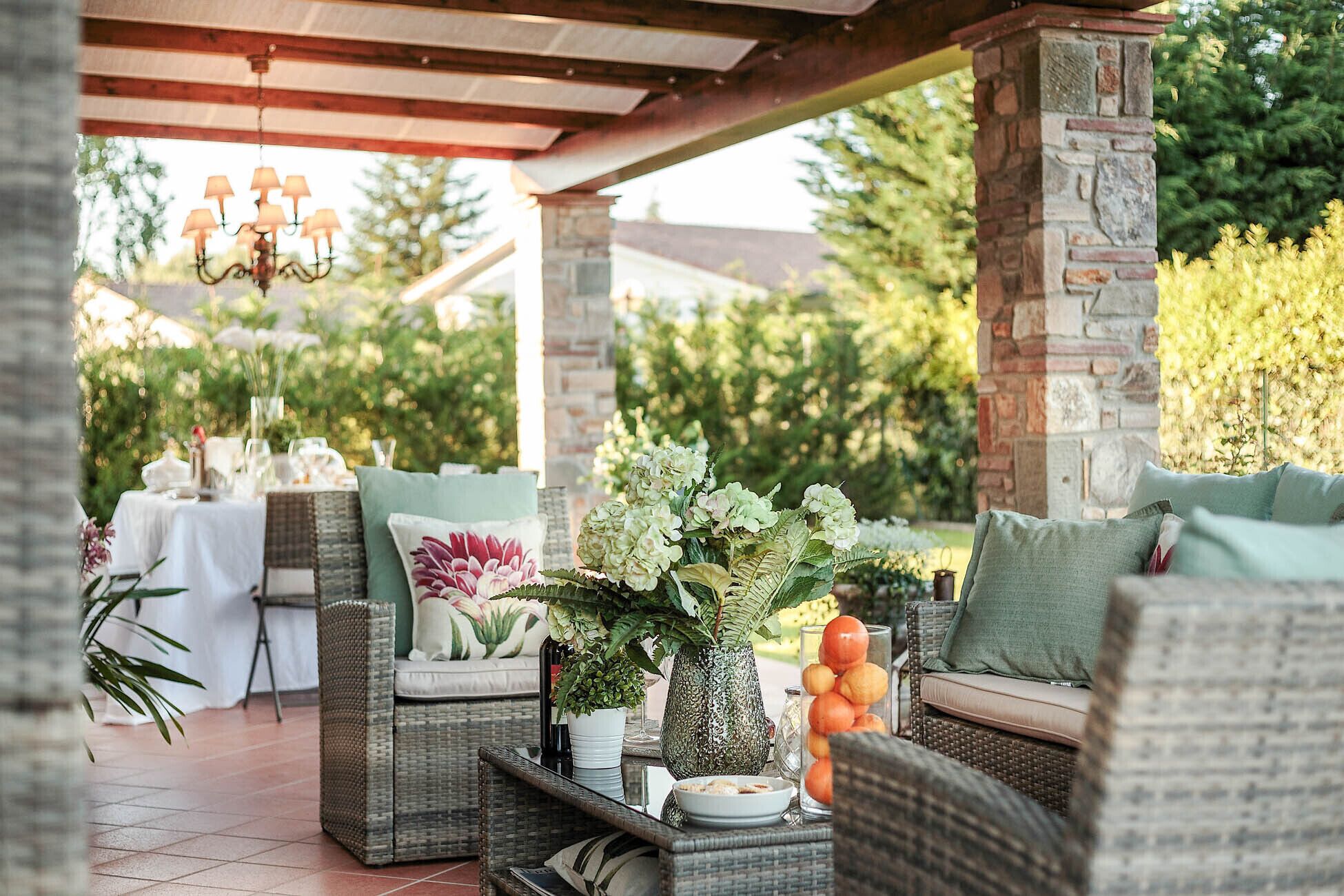 An outdoor patio with wicker furniture, a table set for dining, and a variety of plants and decorative items.