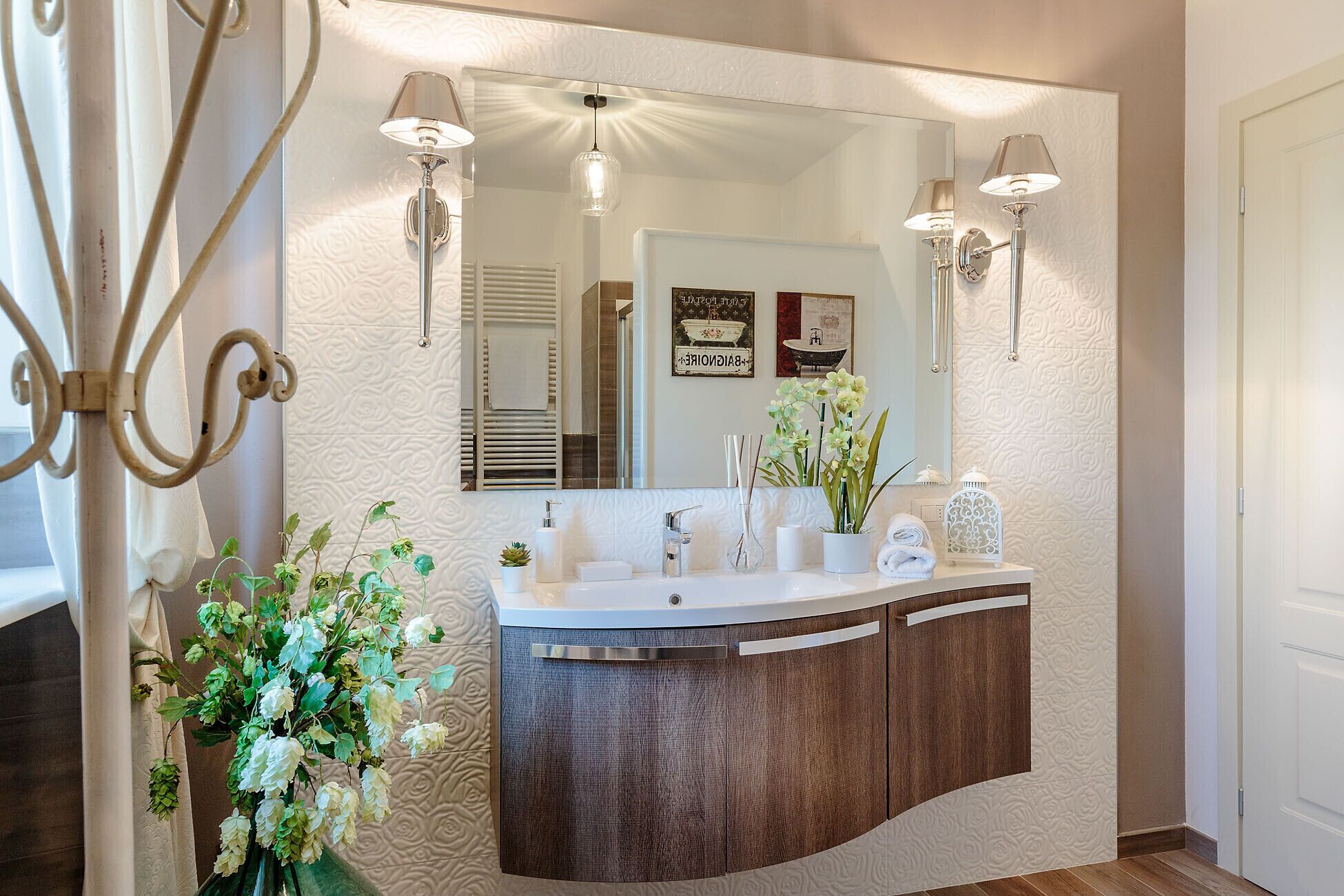 A bathroom with a large mirror, two wall-mounted lights, a sink with a wooden cabinet, and decorative plants.