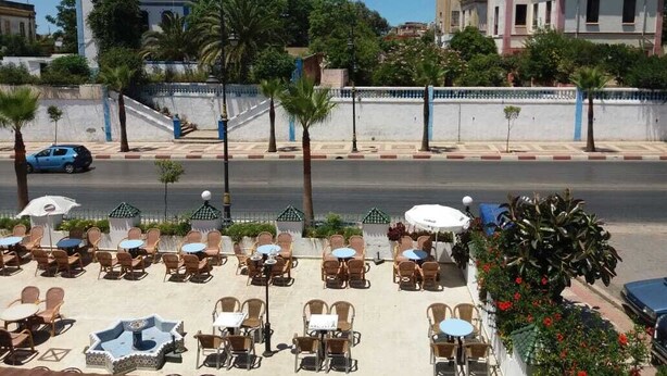 Ein Straßencafé mit Tischen und Stühlen, eine Palme und ein Gebäude im Hintergrund.