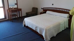 Ein Schlafzimmer mit Bett, einem Sessel, einem Nachttisch, einem Spiegel und einer Wandleuchte.