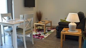 Uma sala de estar com uma mesa de jantar, cadeiras, um sofá, uma televisão, um abajur e um tapete floral.