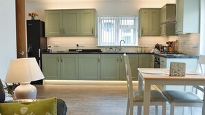 Uma cozinha moderna com armários verdes, um espaço de refeições com mesa e cadeiras, e uma janela com persianas.