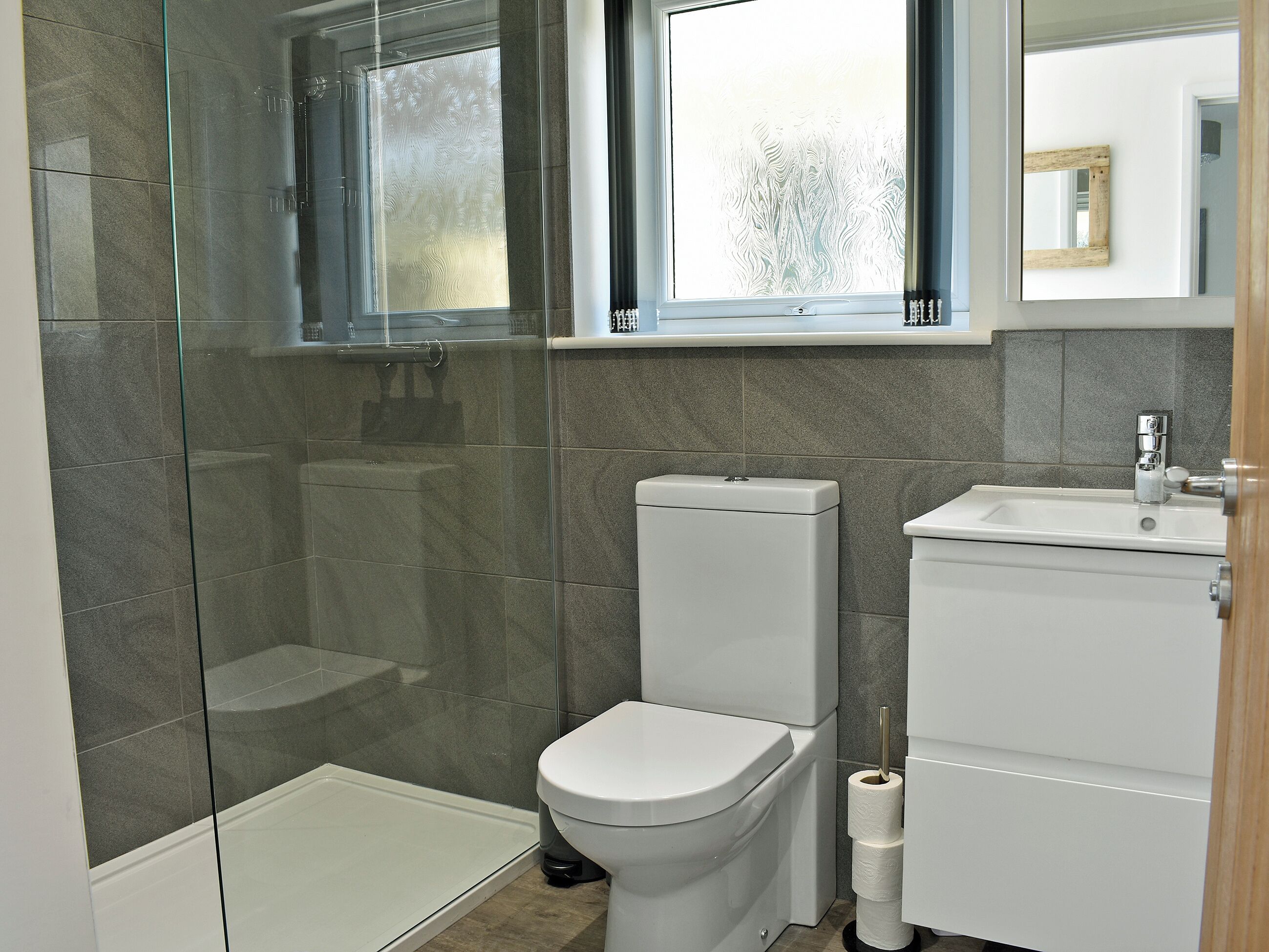 A bathroom with a glass shower enclosure, a toilet, and a sink with a mirror above.