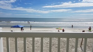 A beach with a white railing, a blue tent, and a colorful umbrella. - Ocean and Pool View Condo – Point East Condominium (New Smyrna Beach)