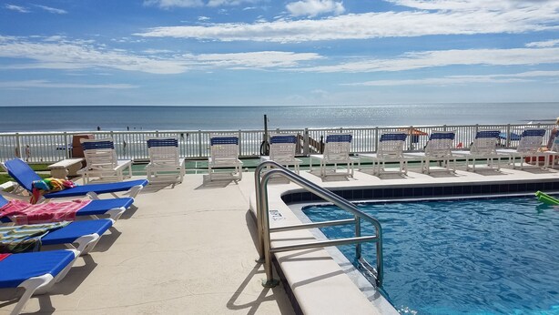 A poolside area with sun loungers and a pool. - Ocean and Pool View Condo – Point East Condominium (New Smyrna Beach)
