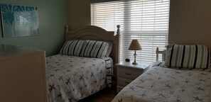 Une chambre avec deux lits, une table de chevet avec une lampe et une fenêtre avec des stores.