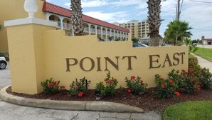 A sign with "POINT EAST" in large letters, surrounded by red flowers and palm trees. - Ocean and Pool View Condo – Point East Condominium (New Smyrna Beach)