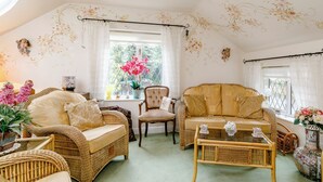 A cozy living room with wicker furniture, a glass coffee table, and a window with a view of greenery.