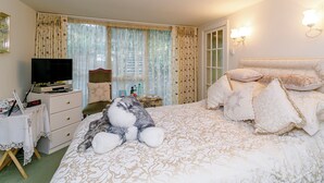 A bedroom with a bed, a television on a dresser, a clock, and a window with curtains.