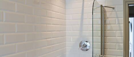 A bathroom with white subway tile walls, a glass shower enclosure, and a chrome showerhead.