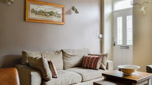 En stue med en beige sofa, et billede i ramme på væggen, et træbord med en skål og et hjortehoved monteret på væggen.