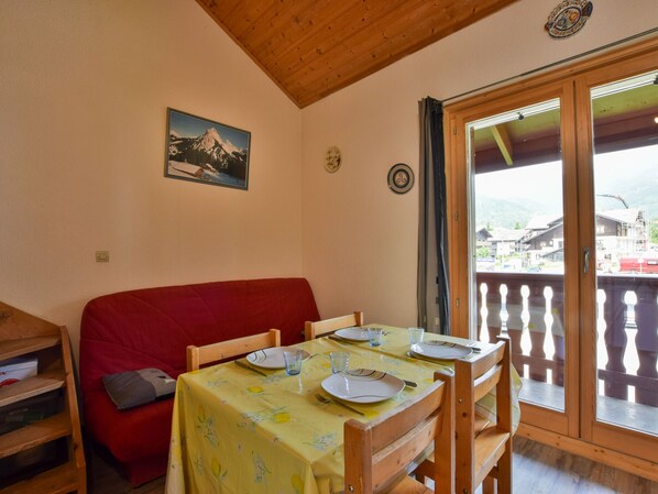 Ein Essbereich mit Tisch für vier Personen, eine rote Couch, Holzsessel, eine Holzzielung, ein Fenster mit Blick auf Gebäude und ein Gemälde von einem Berg an der Wand.