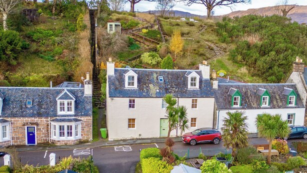 A residential area with houses, a red car parked on the street, and a small shed. - 4 bedroom accommodation in Plockton (Plockton)