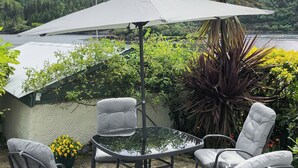A patio with a table and four chairs, an umbrella, and a view of a forested area. - 4 bedroom accommodation in Plockton (Plockton)