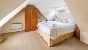 A bedroom with a sloped ceiling, a wooden wardrobe, a bed with white bedding, and a window with a view of greenery. - 4 bedroom accommodation in Plockton (Plockton)