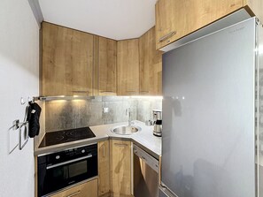 A compact kitchen with wooden cabinets, a stainless steel refrigerator, a built-in oven, a dishwasher, and a coffee maker.