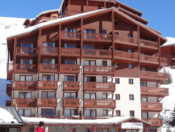 Un edificio de madera de varios pisos con balcones, probablemente un hotel o albergue, rodeado de nieve.