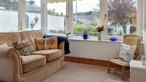 A cozy room with a beige sofa, a wooden chair, and a window with a view of the outside.