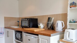 A compact kitchen with a microwave, toaster, kettle, and a cutting board on the counter.