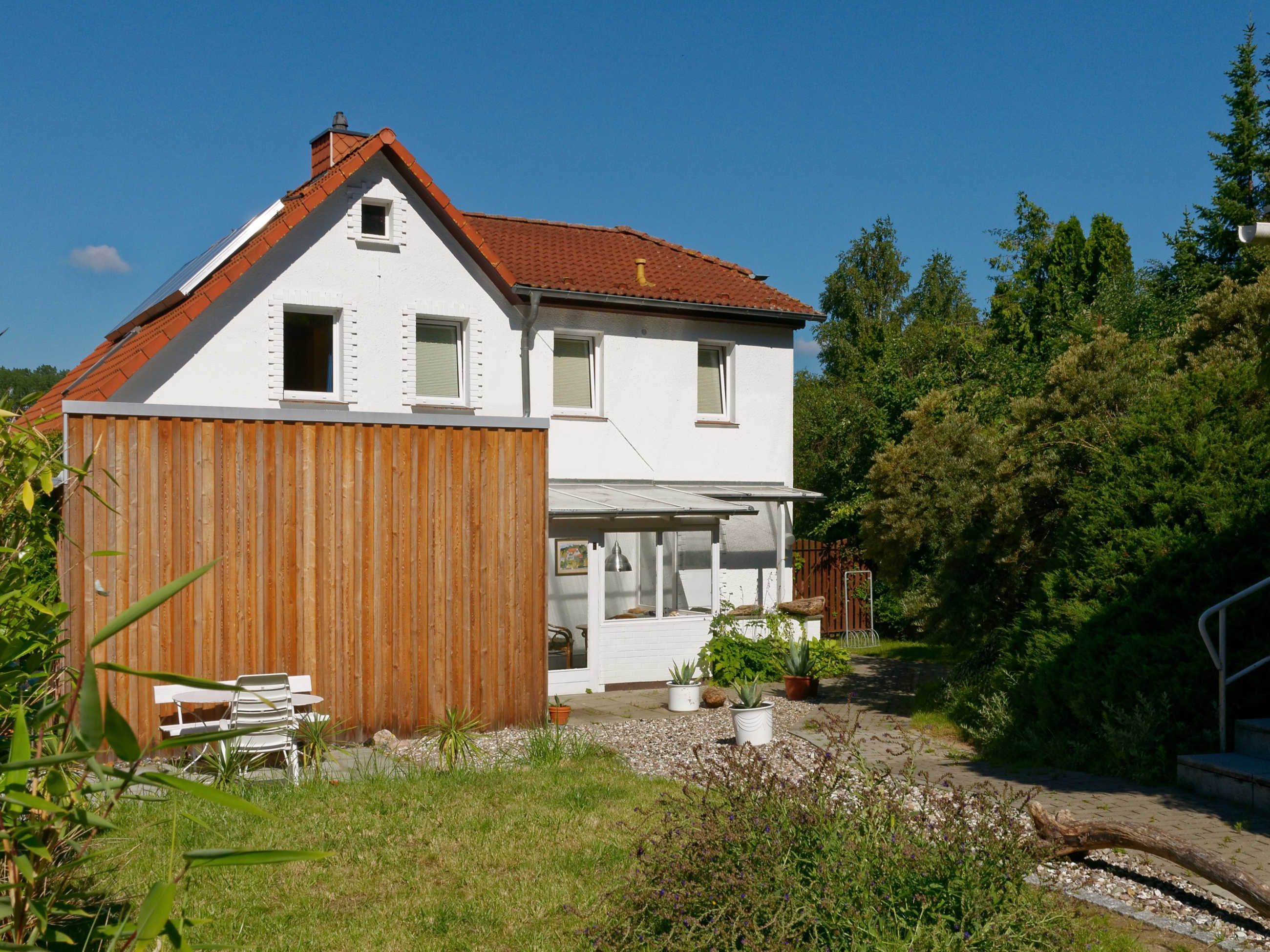A two-story house with a sloped roof, a wooden fence, and a garden with potted plants.