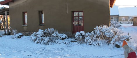Yhden kerroksen rakennus, jossa on punainen ovi ja ikkunat, ja sen ympärillä on lumipeitteistä maata ja pensaita.
