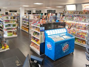 A grocery store with shelves stocked with various products, a blue Nestle cooler, and signs indicating different sections like Baby/Hygiene and Kaffe/Tea/Bed.