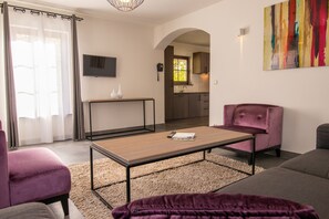 En moderne stue med sofa, lænestol, sofabord og kig til køkkenet.