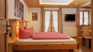 Una cama de madera con ropa de cama de cuadros rojos, un televisor en la pared y un escritorio de madera.