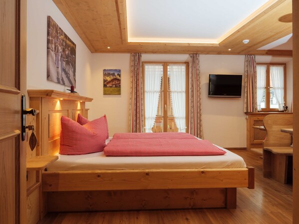 Una cama de madera con ropa de cama de cuadros rojos, un televisor en la pared y un escritorio de madera.