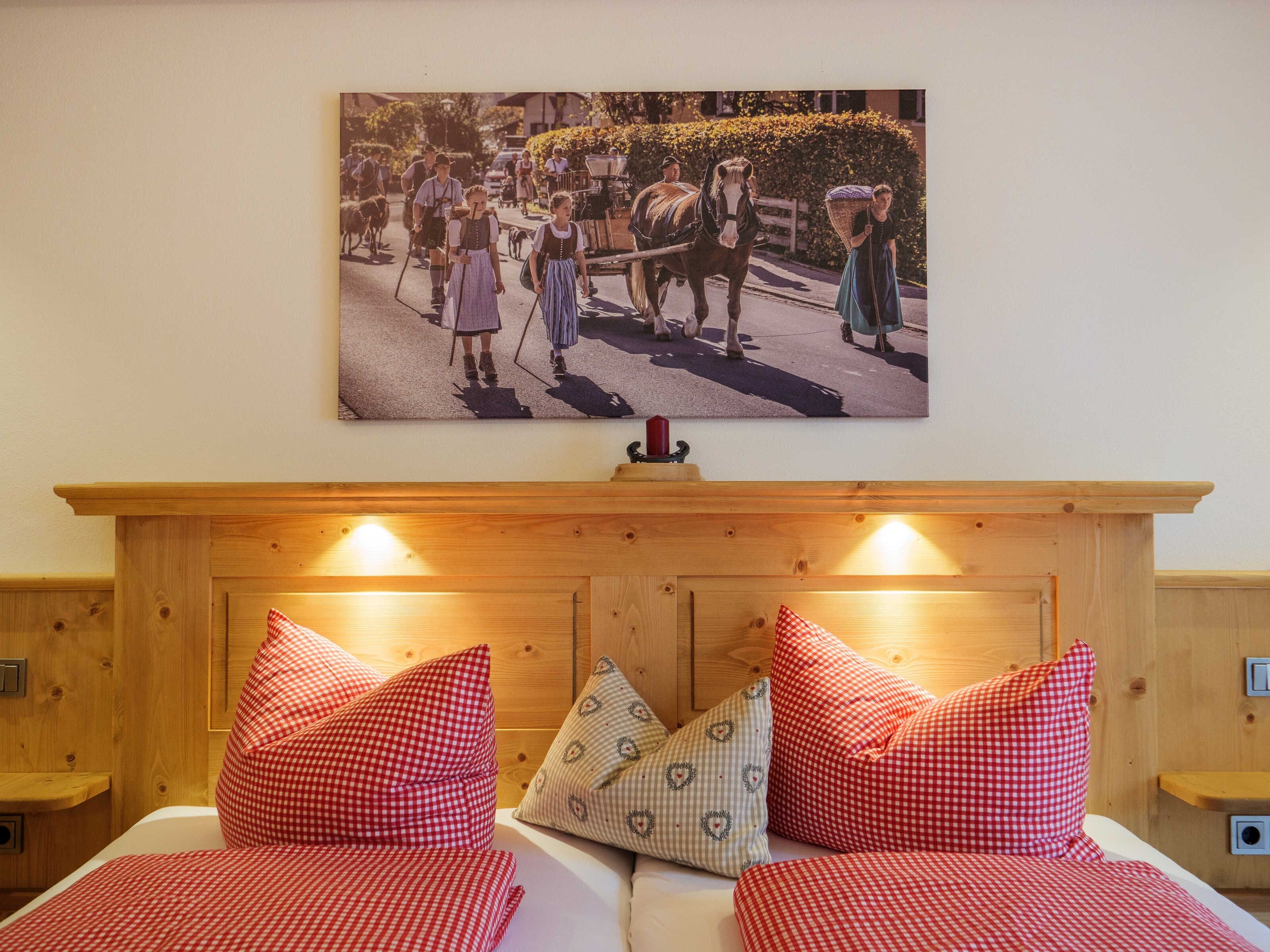 Une chambre à coucher avec une tête de lit en bois, deux lits avec une literie à carreaux rouges et blancs, et un tableau représentant une scène historique accroché au mur.