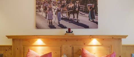 A bedroom with a wooden headboard, two beds with red and white checkered bedding, and a wall-mounted picture of a historical scene.