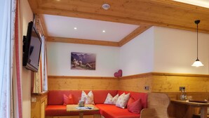 Una habitación acogedora con techo de madera, un sofá rojo con cojines estampados, una pequeña mesa de madera y un televisor montado en la pared.