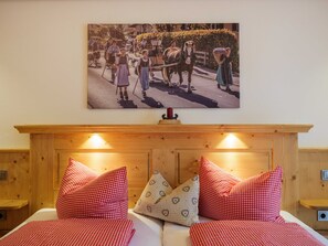 Un dormitorio con cabecera de madera, dos camas con ropa de cama a cuadros rojos y blancos, y un cuadro de escena histórica colgado en la pared.