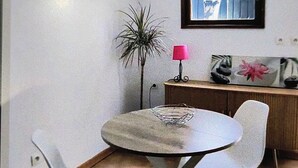 A small dining area with a round table, two chairs, a floor lamp, and a cabinet with decorative items.