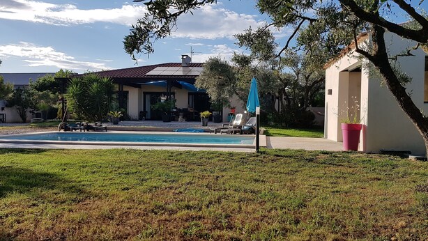 A swimming pool with lounge chairs, a small building with a tiled roof, and surrounding greenery.