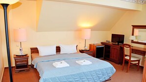 Une chambre d’hôtel comprenant un lit, deux tables de chevet, un bureau, une chaise, une télévision et des lampes.