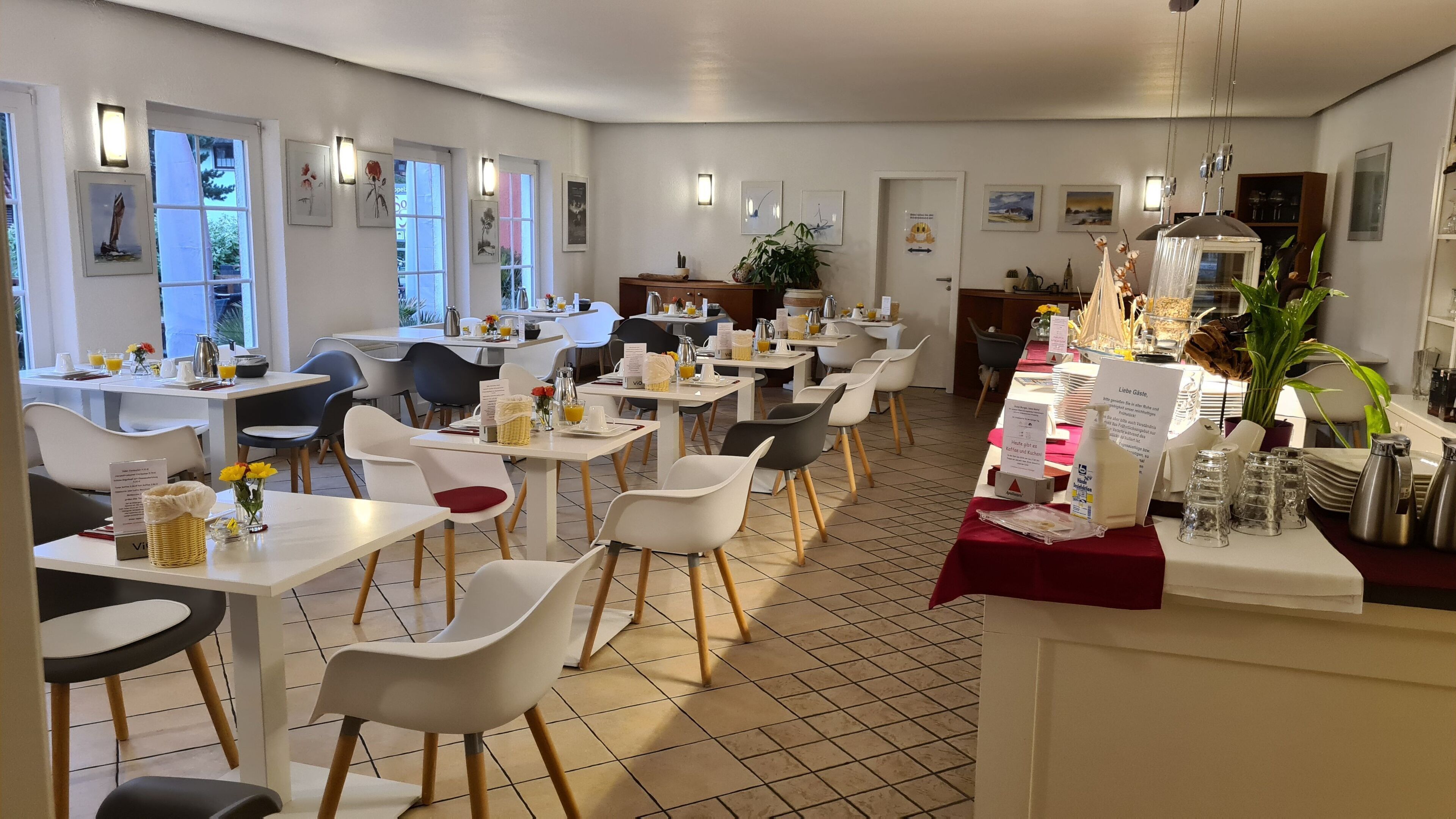 Et moderne spiseområde med hvide borde og stole, et buffetbord og kunst på væggene.
