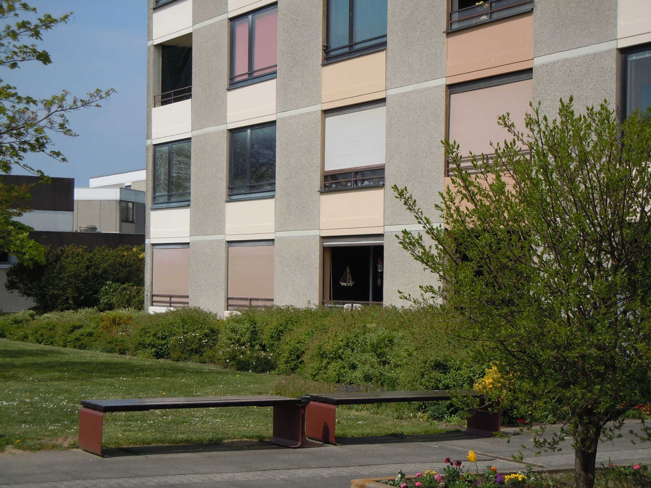 A modern building with a flat roof, large windows, and a bench in the foreground.