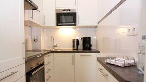 A compact kitchen with white cabinets, a built-in oven, a microwave, and a coffee maker. - Baltic Sea Apartment App. 6110 - Baltic Sea app. App. 6110 (Wendtorf)