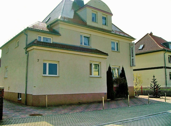 A two-story building with a flat roof, a small balcony on the second floor, and a sign indicating it is a pension home.