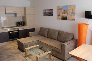 A modern living area with a sofa, coffee table, and a kitchen with cabinets and appliances. - Vacation apartment 6 - Ferienwohnungen Hoffmann (Binz)