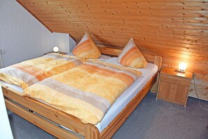 Una cama de madera con una colcha a rayas y almohadas, una mesita de noche con una lámpara y un cabecero de madera.