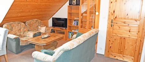 A cozy living room with a sofa, a coffee table, and a television. There is a wooden cabinet with glass doors and a wooden door.