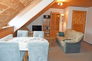 Acogedor cuarto ático con una mesa de comedor, sillas, un sofá, un televisor, una estantería y una puerta de madera.