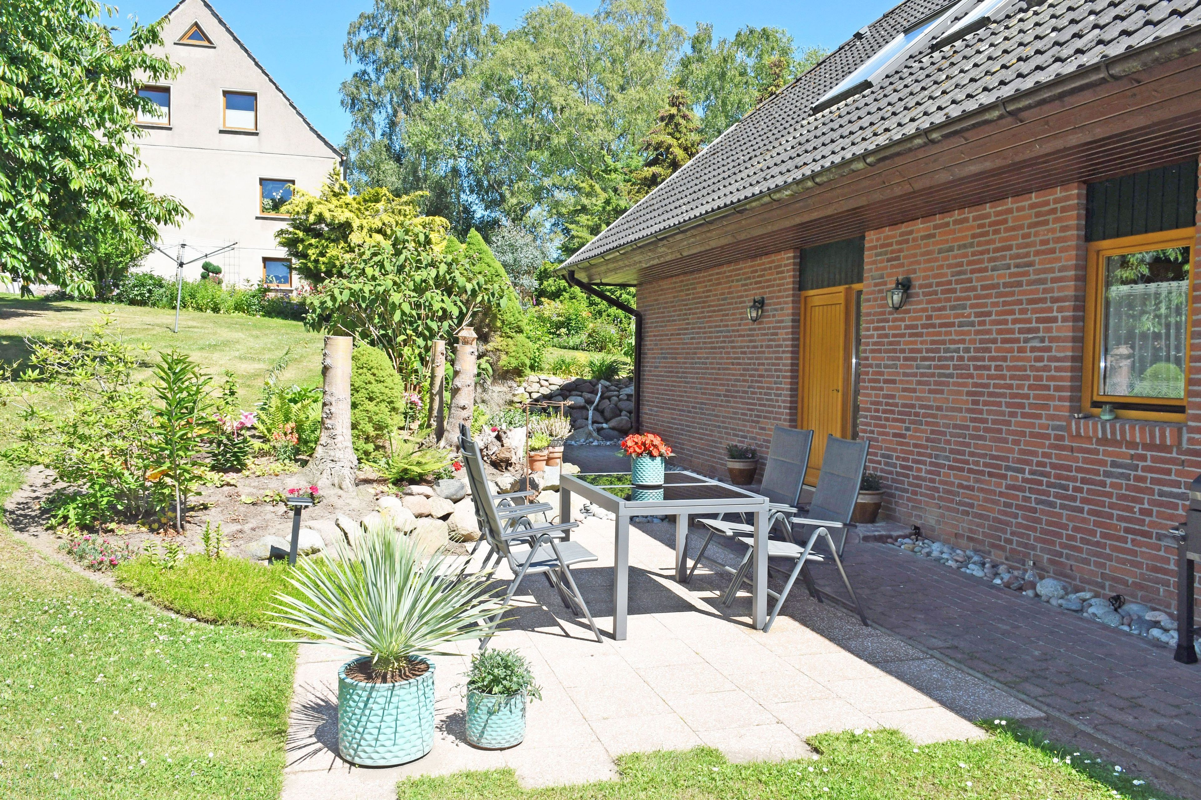 A brick house with a tiled roof, a garden with potted plants, and a patio with outdoor furniture.