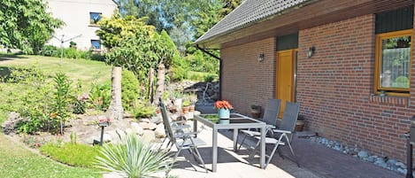 A brick house with a tiled roof, a garden with potted plants, and a patio with outdoor furniture.
