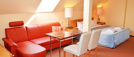 A hotel room with a glass table, red leather sofa, white chairs, a bed, and a skylight.