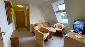 Una habitación con sofá, una mesa pequeña, televisor y ventana.